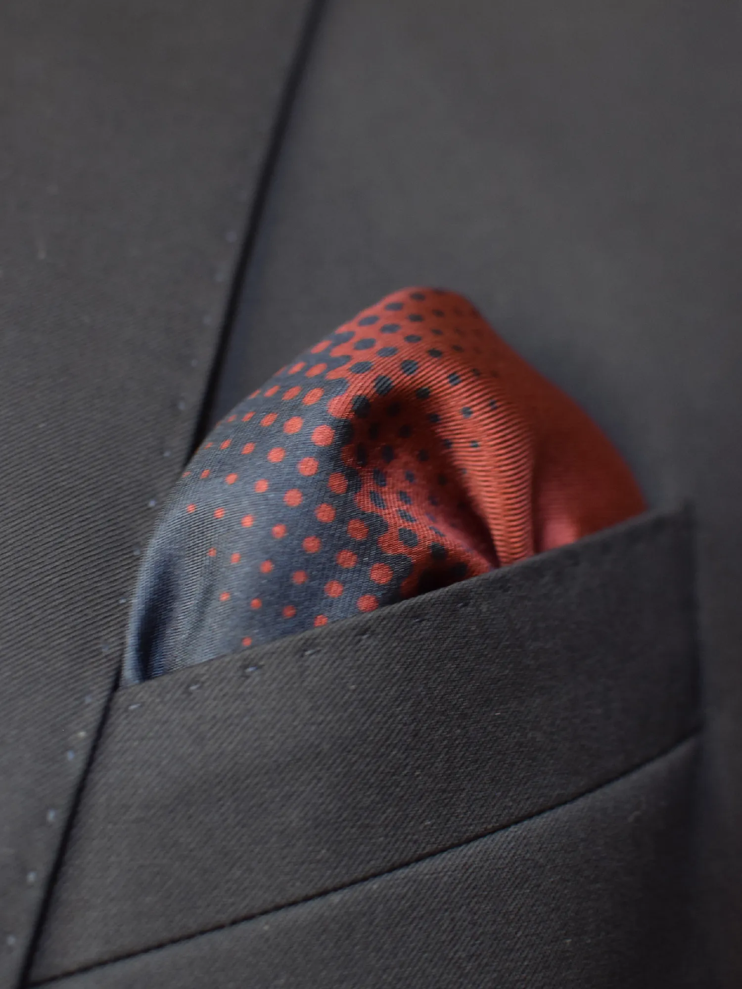 Pochette Lanvin portée en pli bouffant dans une veste sombre, dévoilant le jeu de pois rouges sur fond noir.