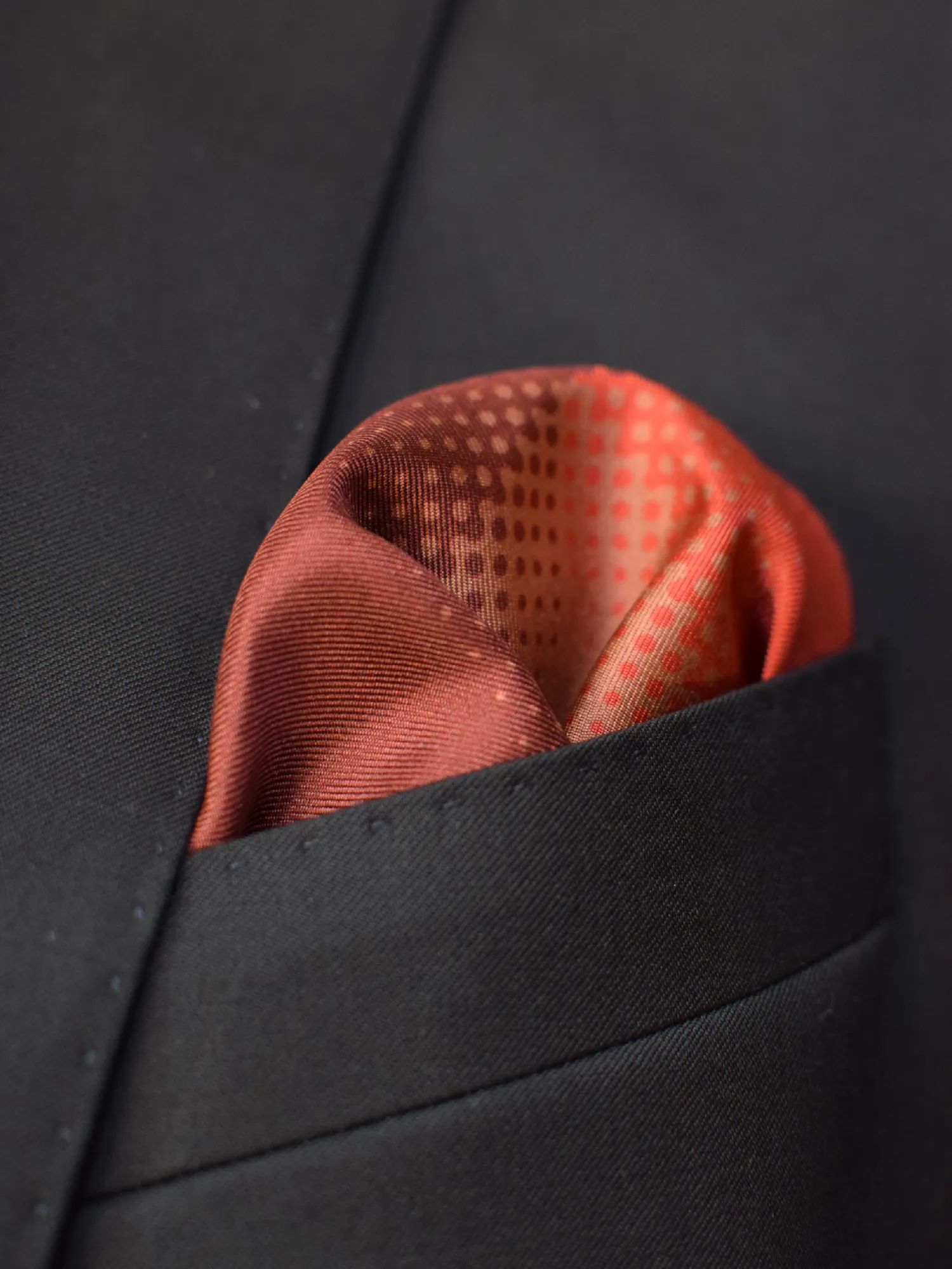 Pochette Lanvin en soie dans une poche de veste, en pli bouffant, montrant les couleurs rouille, marron chaud et orange.