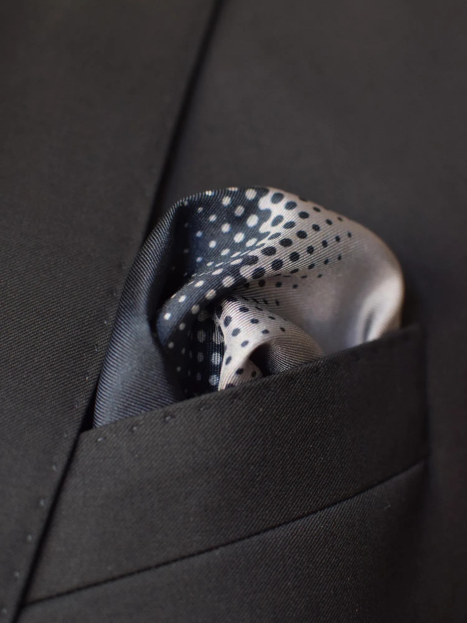 Pochette Lanvin gris à pois, portée dans une veste foncée, en pli bouffant.