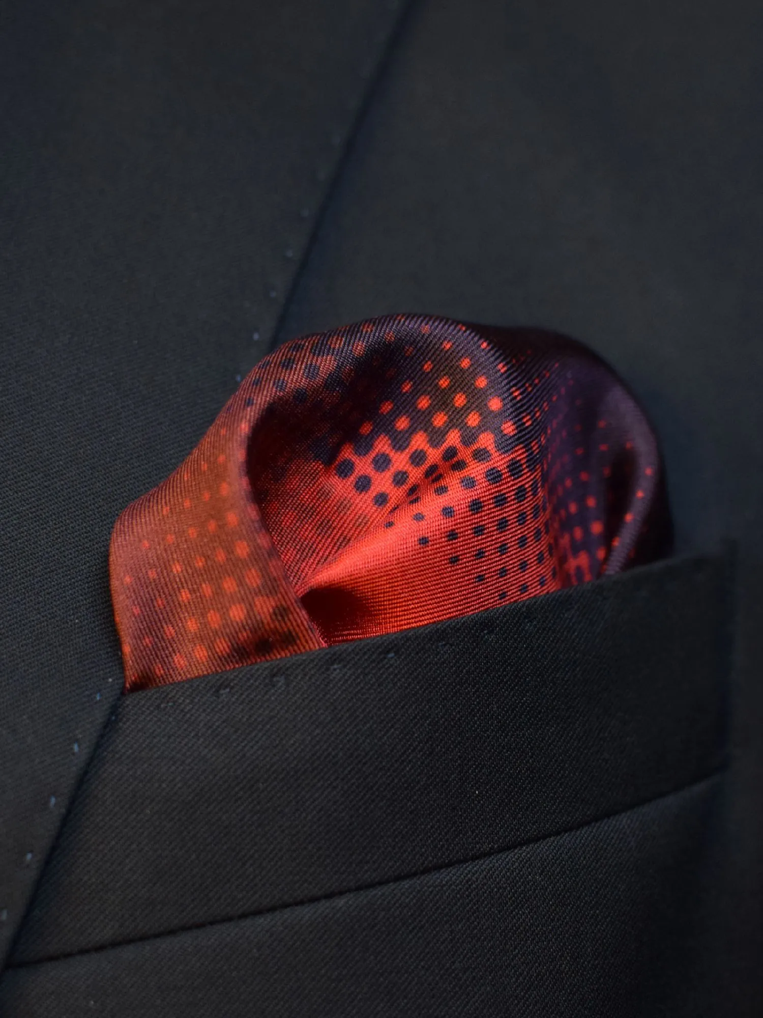 Pochette de costume Lanvin en soie rouge et bordeaux à quatre panneaux, glissée dans la poche poitrine d’une veste sombre.