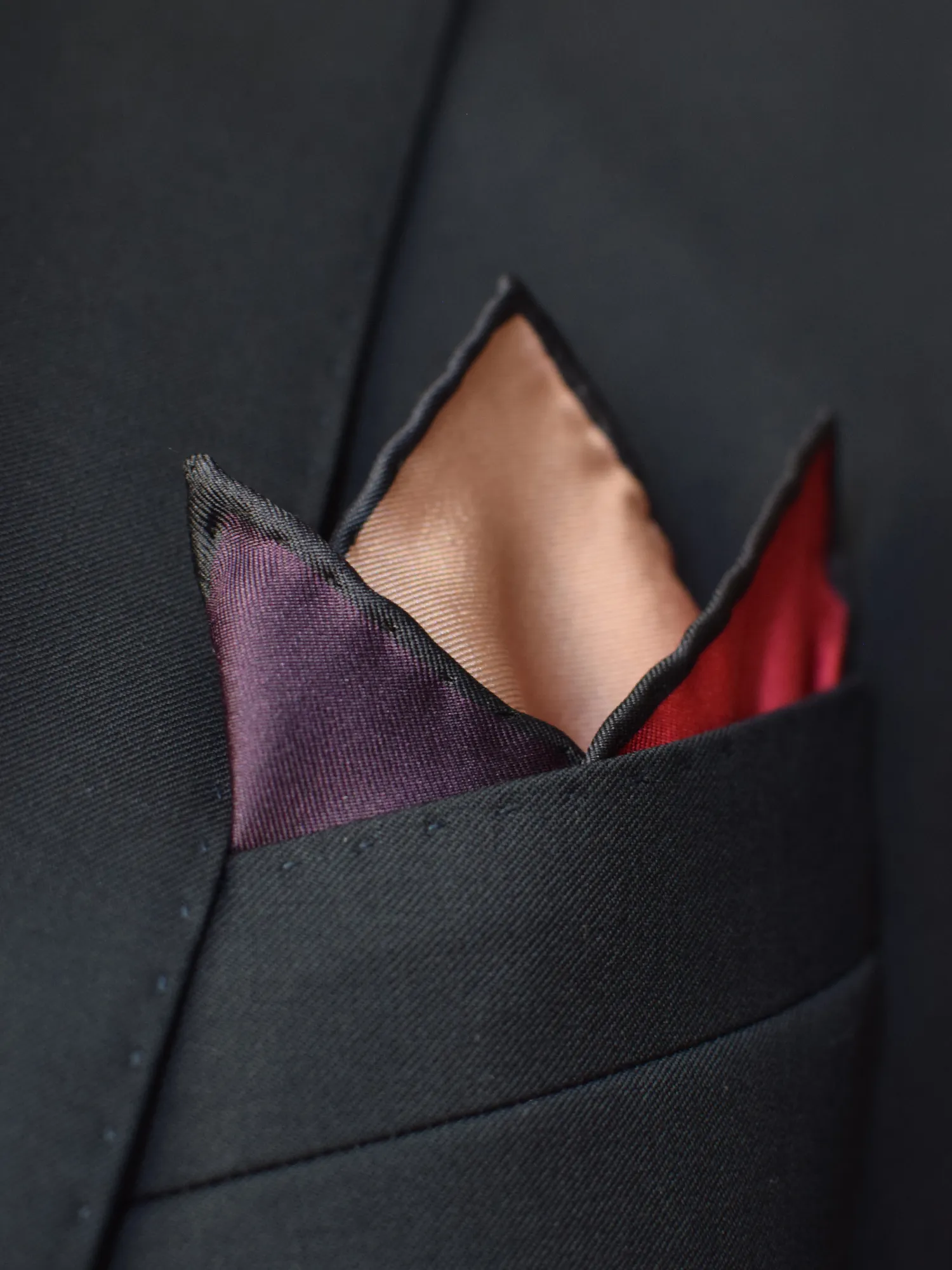 Pochette Lanvin dans une poche de veste, pli en trois pointes, exposant les teintes violet, beige et rouge.