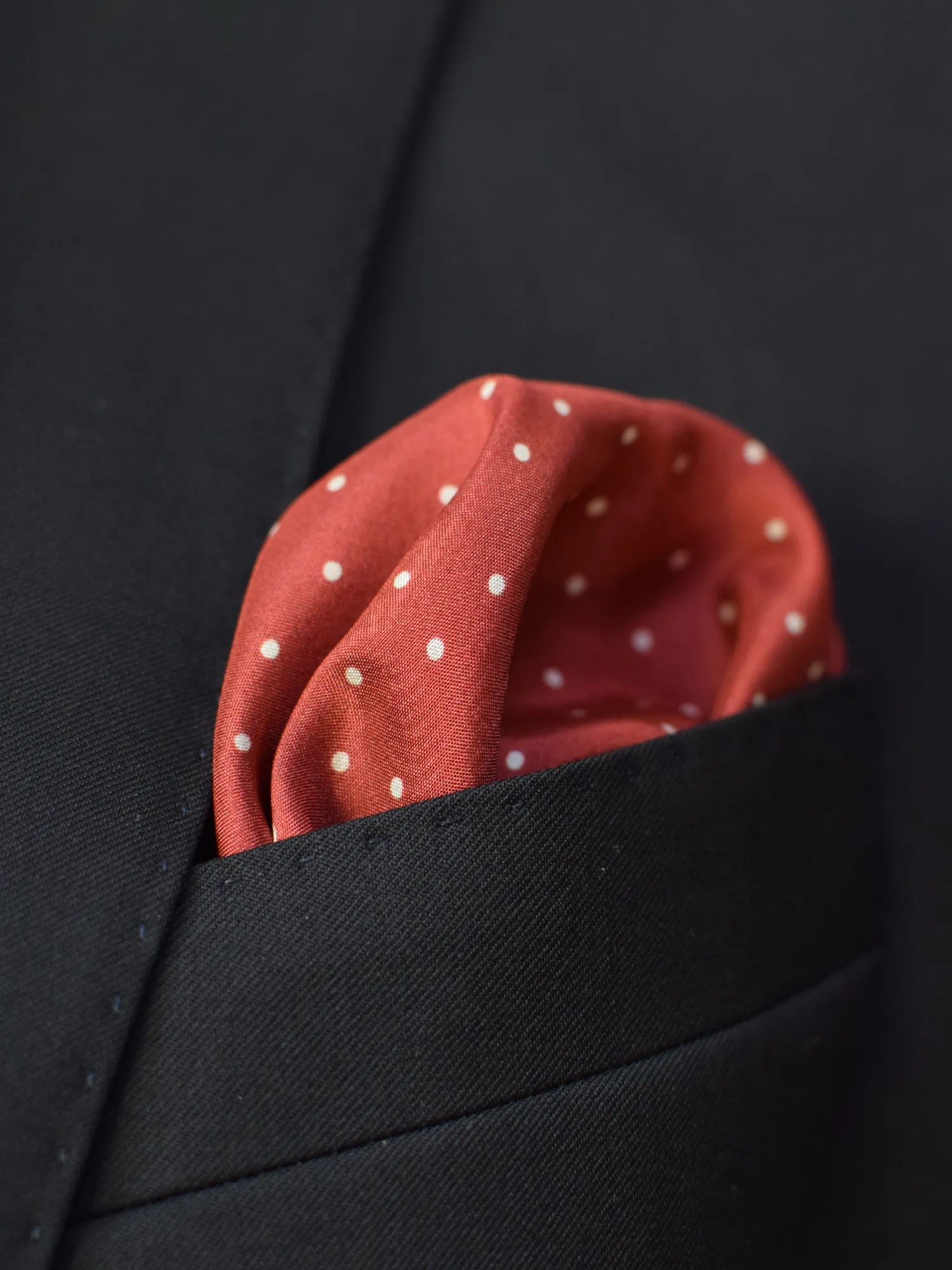 Pochette Lanvin rouge fraise à pois blancs en soie, portée dans une veste noire.